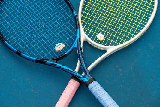 Two rackets crossed on court, each with a Pupcourt dampener in the strings and a Pupcourt overgrip on the handle