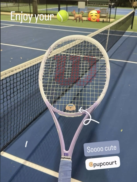 A customer's Wilson racquet with a Pupcourt Golden Retriever dampener in the strings and a Pupcourt overgrip on the handle, on a night hard court