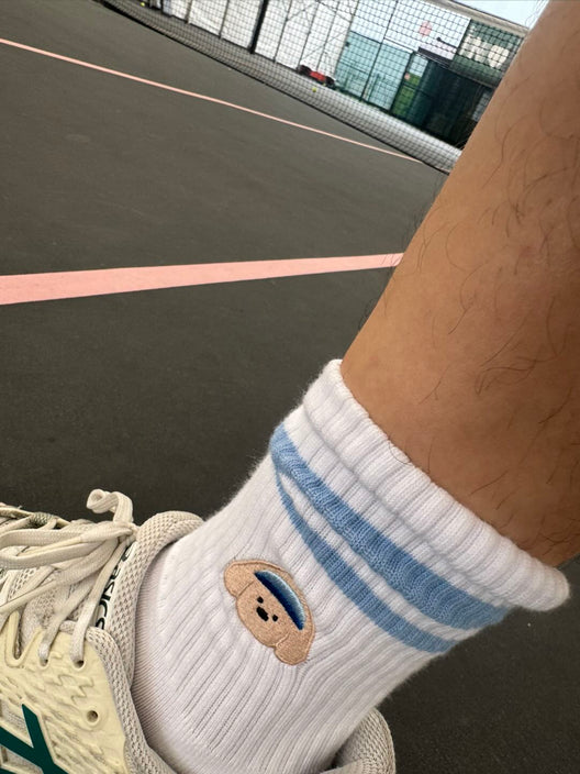 Pupcourt crew socks with the golden retriever embroidery, worn with tennis shoes on a hard court