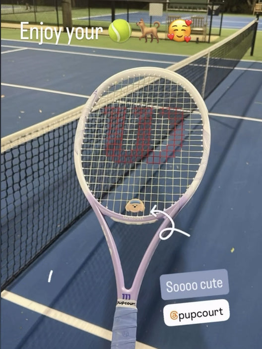 A customer's Wilson racquet with a Pupcourt Golden Retriever dampener in the strings and a Pupcourt overgrip on the handle, on a night hard court